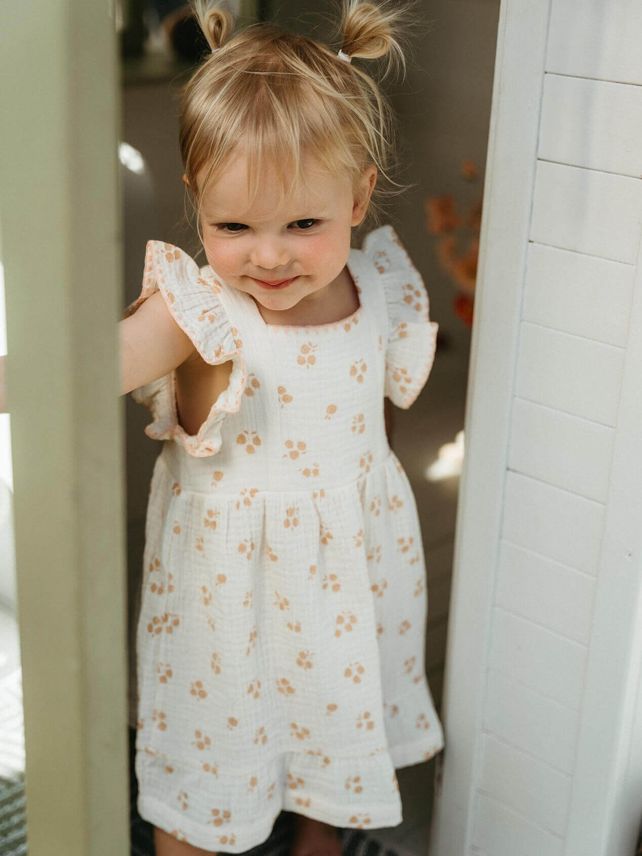 Young girl wearing a white dress with floral patterns in front of a mirror. Amelia Dress - Petal Paws Baby girl