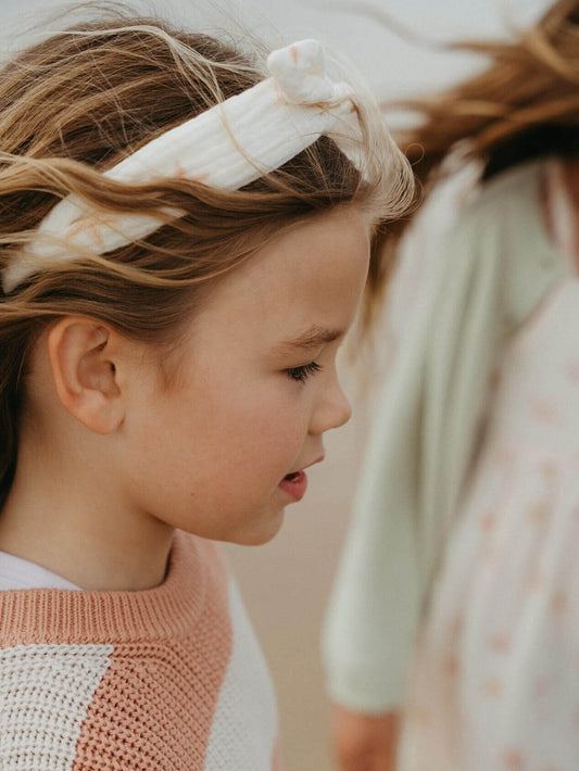 Young girl wearing a headband with another person partially visible in the foreground.