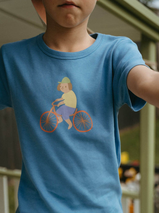 Child wearing a blue t-shirt with a graphic of a person on a bicycle.