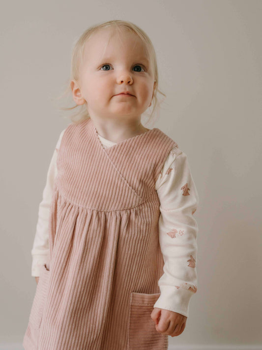 Young child wearing a pink dress over a white shirt with floral patterns against a plain background Baby Corduroy Dress - Blush Baby girl