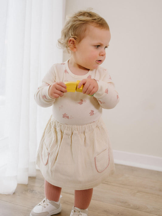 Child in a white dress holding a yellow object indoors Baby Corduroy Skirt - Ecru Baby girl
