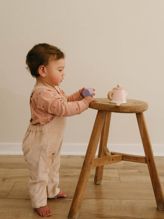 Child playing with toys on a wooden stool against a plain wall. Corduroy Overalls - Clay Baby boy
