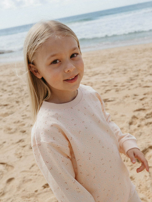 Young girl in a light pink sweater standing on a sandy beach with ocean in the background