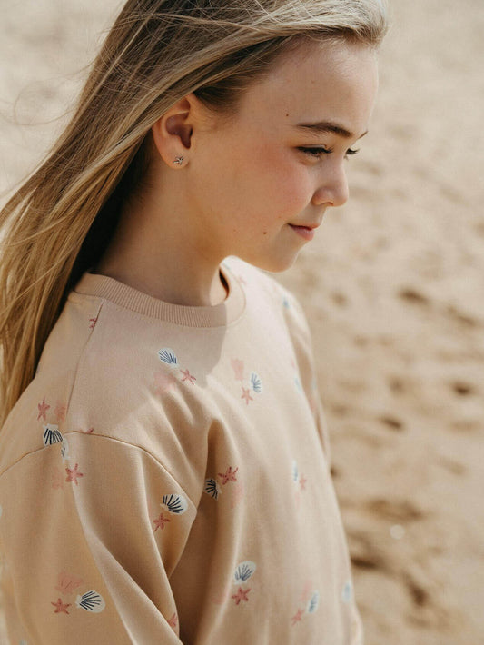 Girl wearing a beige sweater with shell patterns on a blurred beach background