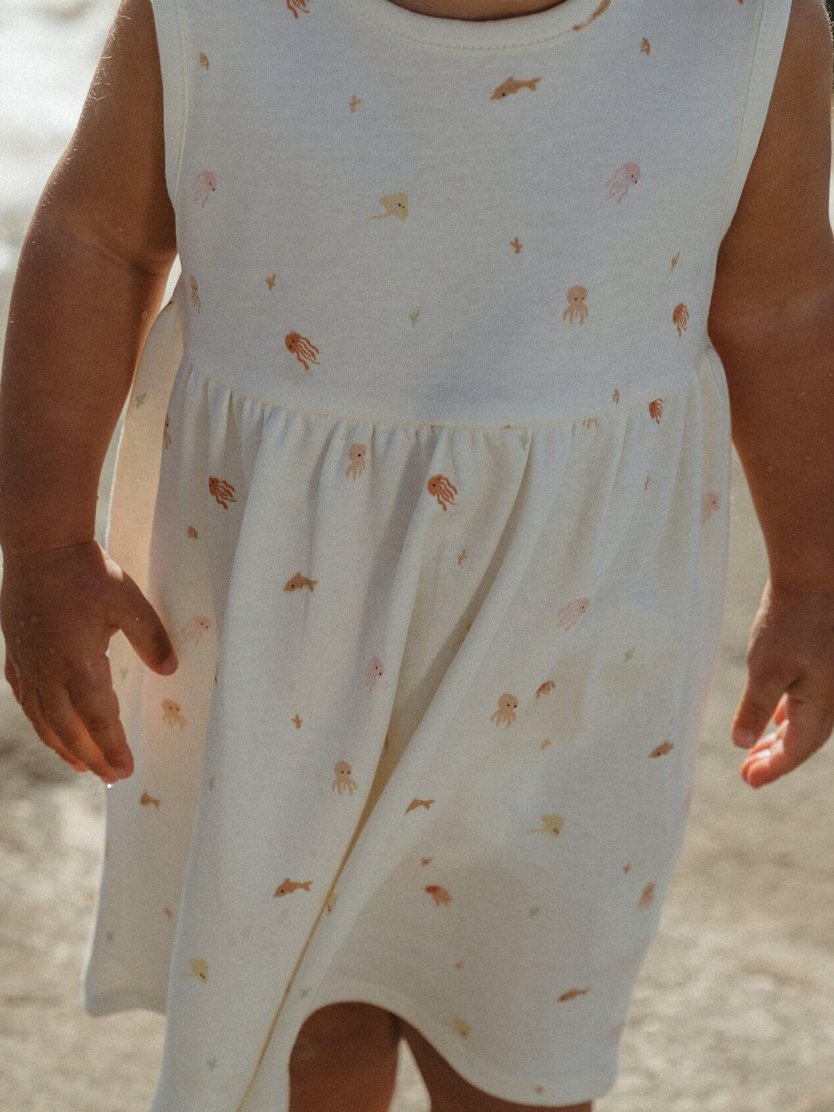 White sleeveless dress with small patterns worn by a child, against a neutral background Jasmine Dress - Ocean Buddies Baby girl