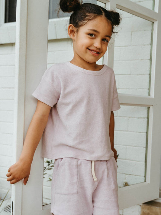 Young girl in a pink outfit standing in front of a white wooden door.