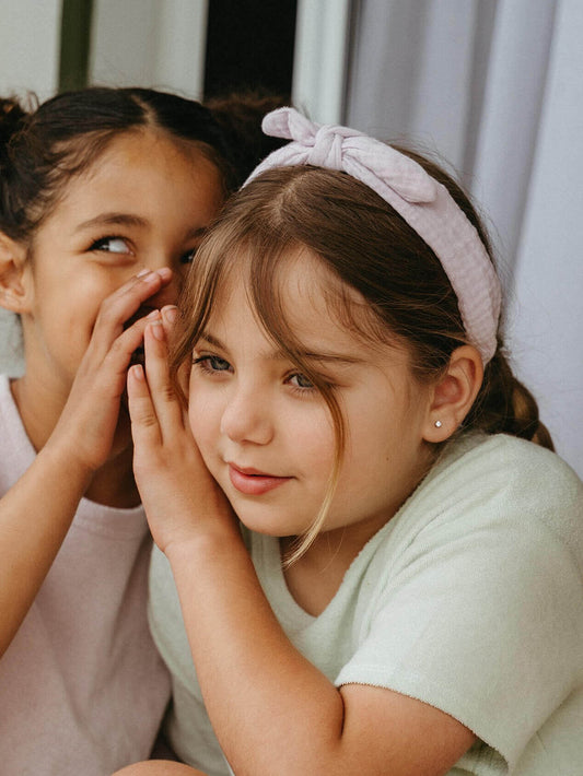 Two young girls with one whispering to the other's ear indoors.