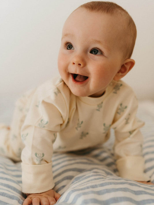 Baby wearing a cream-colored onesie with small patterns, sitting on a striped blanket.