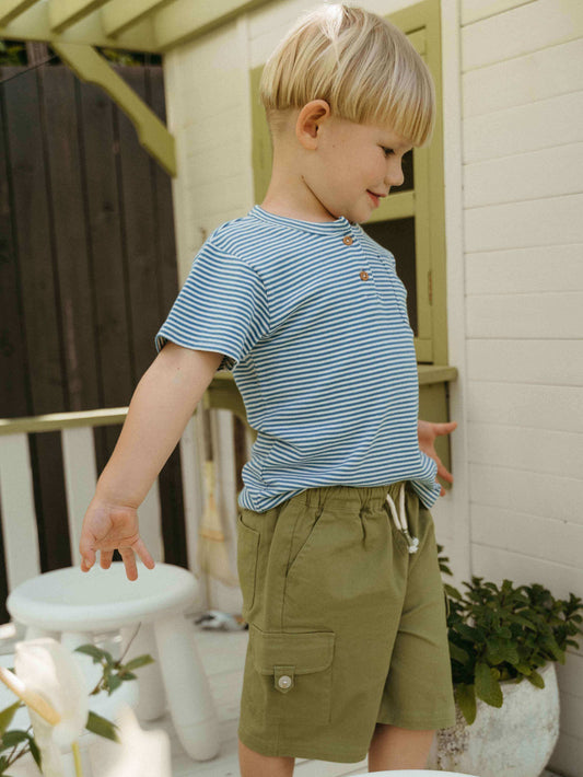 Child wearing a striped shirt and green shorts standing outdoors.