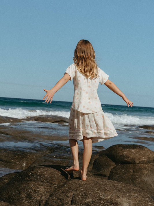 Girl in a dress standing on rocks by the ocean with arms outstretched