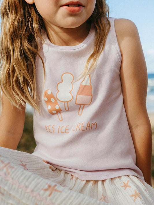Child wearing a pink sleeveless shirt with ice cream graphics and text, sitting outdoors.