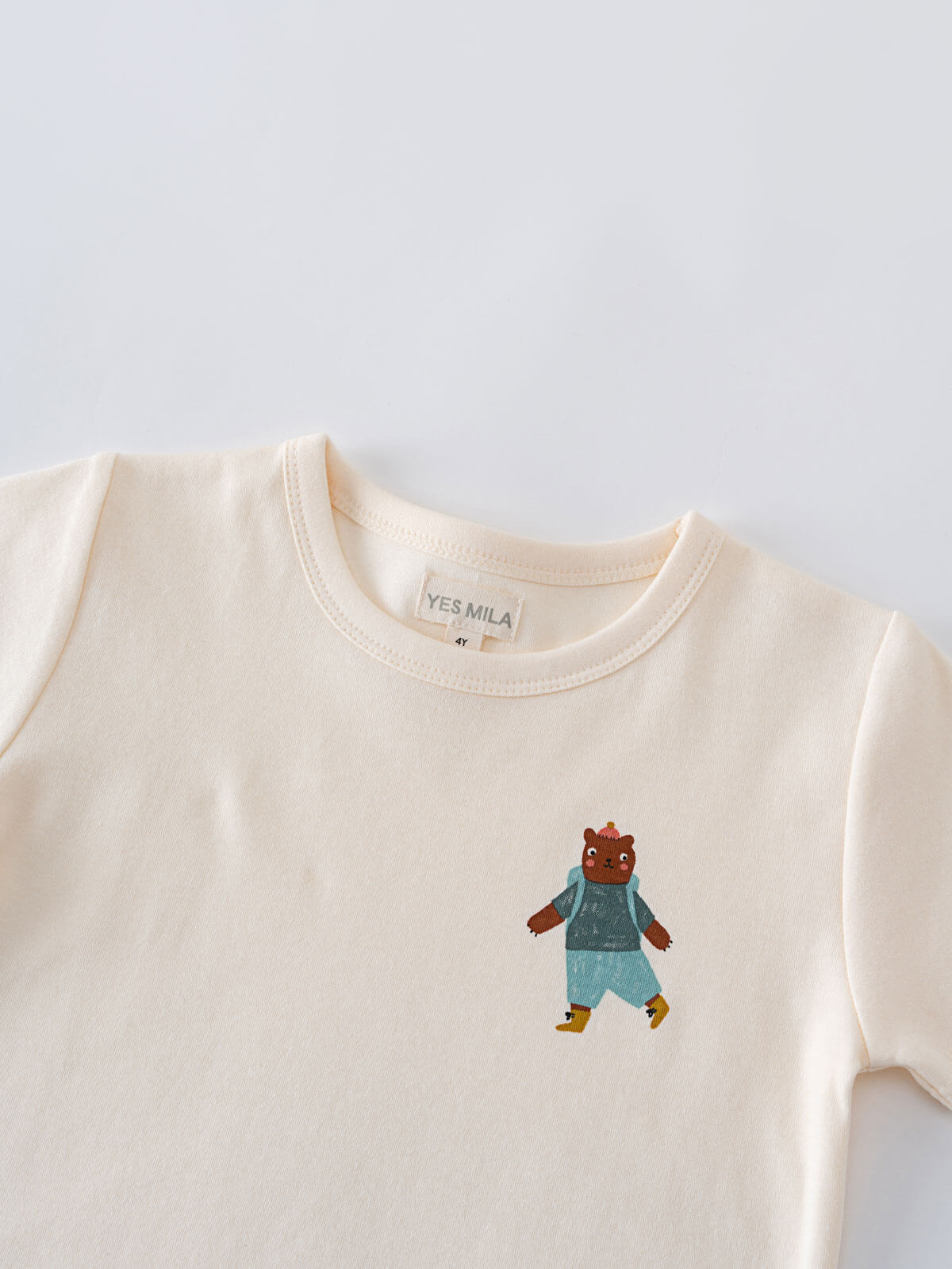 Cream-colored shirt with embroidered bear wearing blue clothing and yellow shoes Feature Print Short Sleeve Tee - Hiking Bear Boys