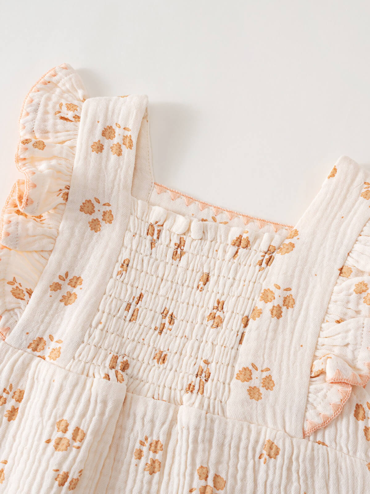 Close-up of white smocked baby romper with orange floral print and ruffled straps Muslin Romper - Petal Paws Baby girl