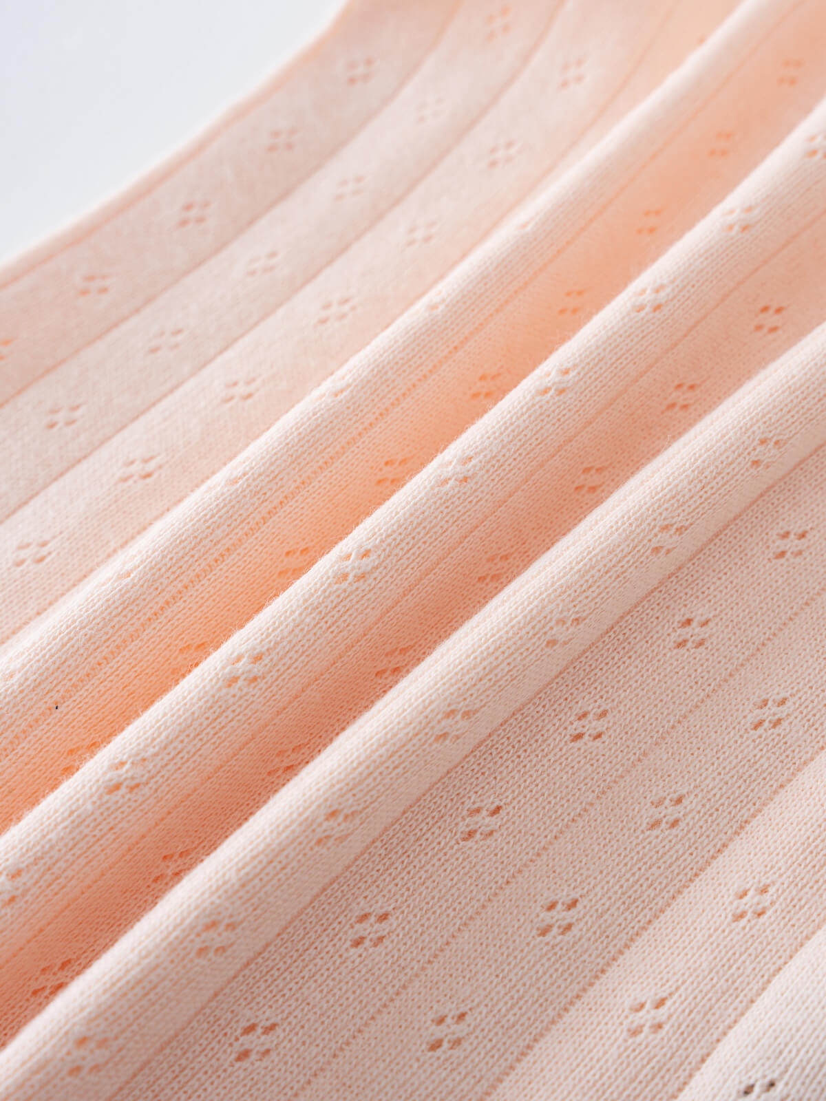 Close-up of peach-colored ribbed fabric with small eyelet pattern details Pointelle Singlet Bodysuit - Shell Pink Baby girl