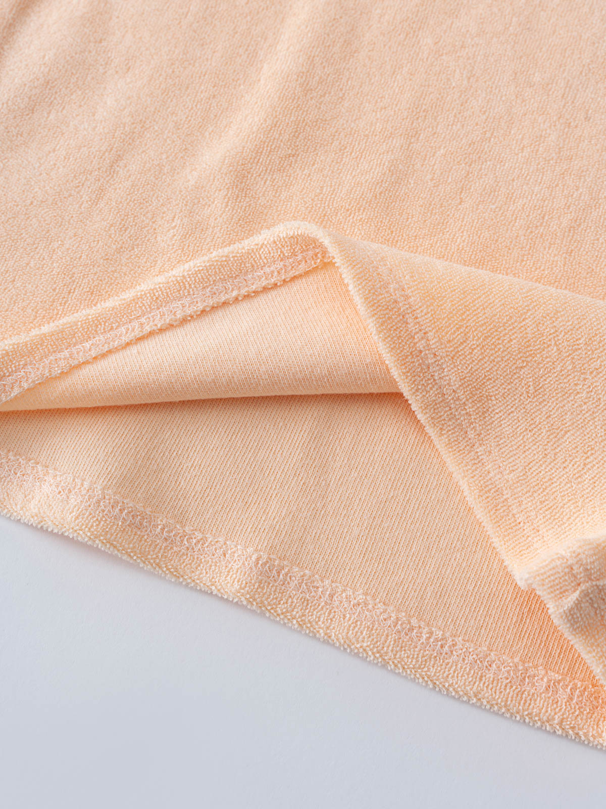 Close-up of peach terry cloth fabric with folded edge showing texture Riley Towelling Tee - Apricot Baby girl