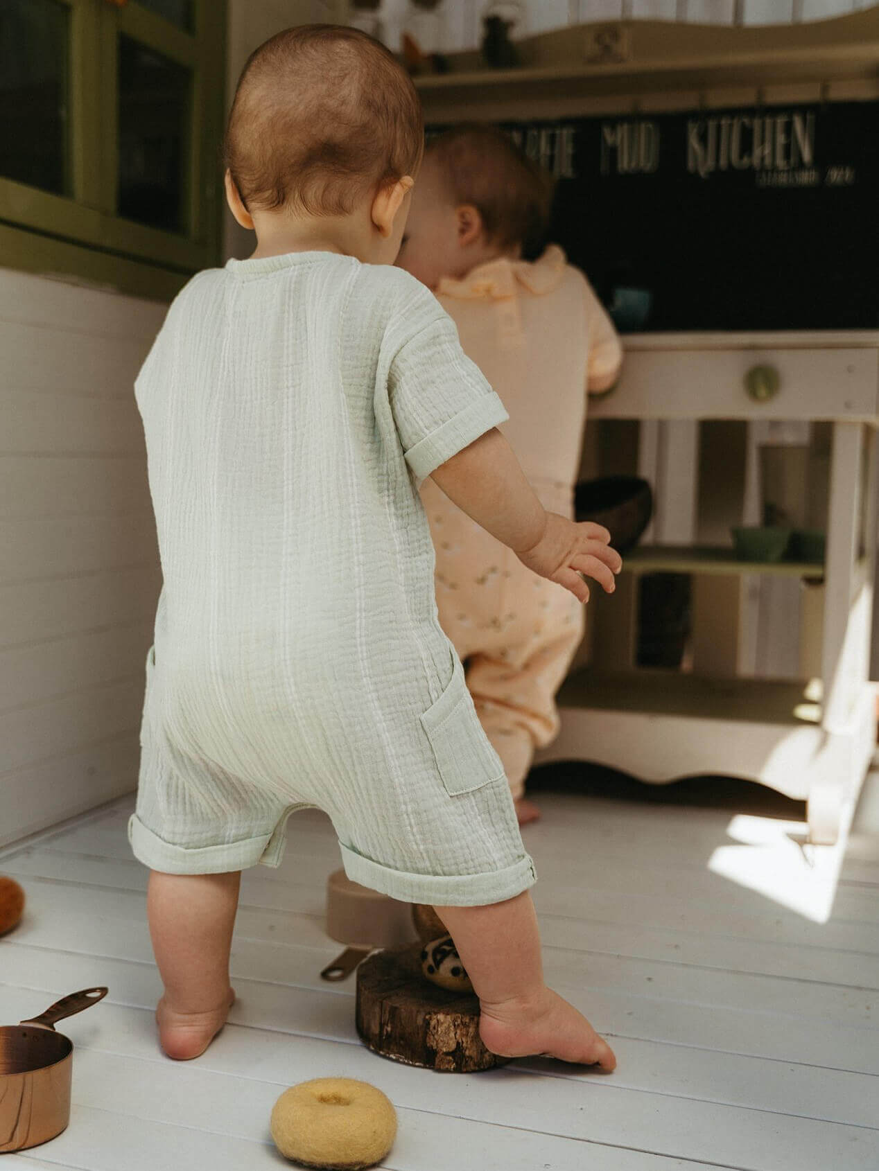 Two babies in a room with wooden floors and furniture. Ryan Romper - Light Green Stripe Baby boy
