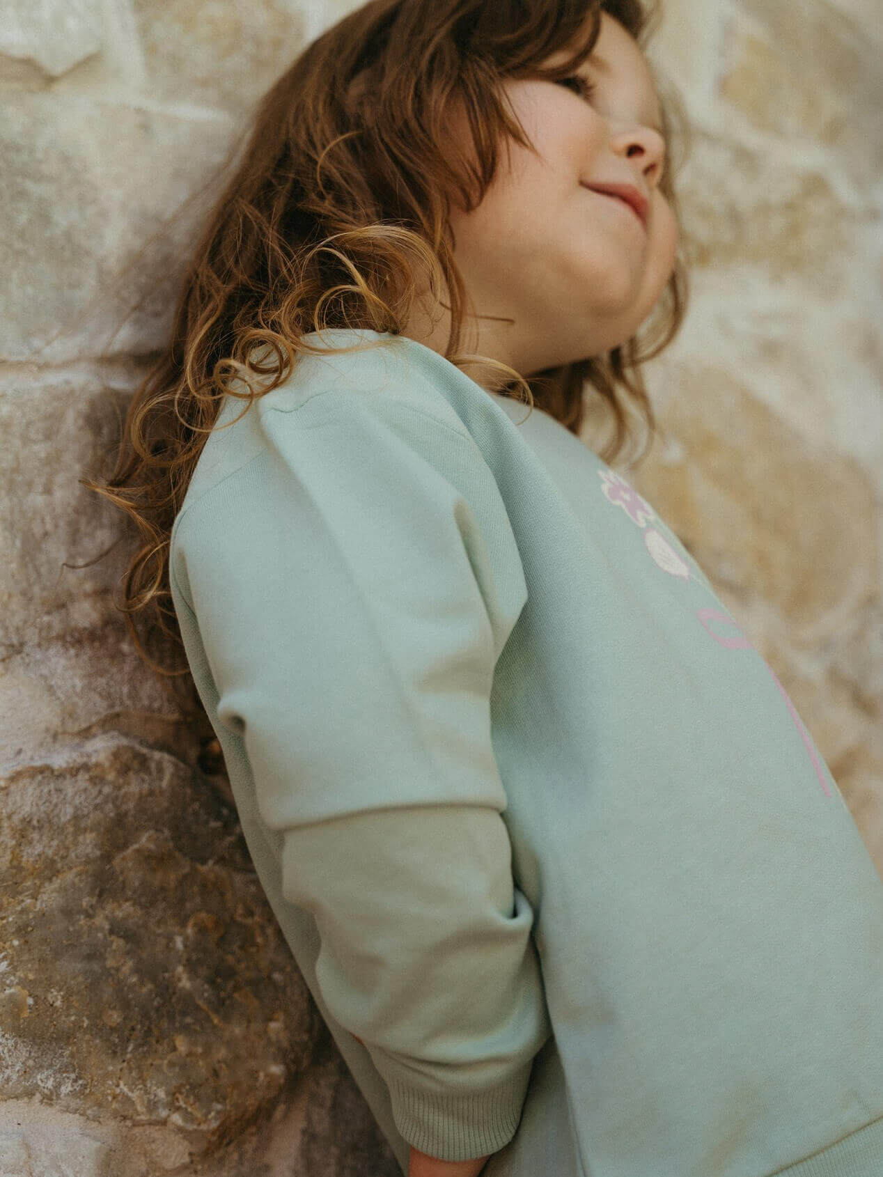 Child wearing a light green sweater against a stone wall