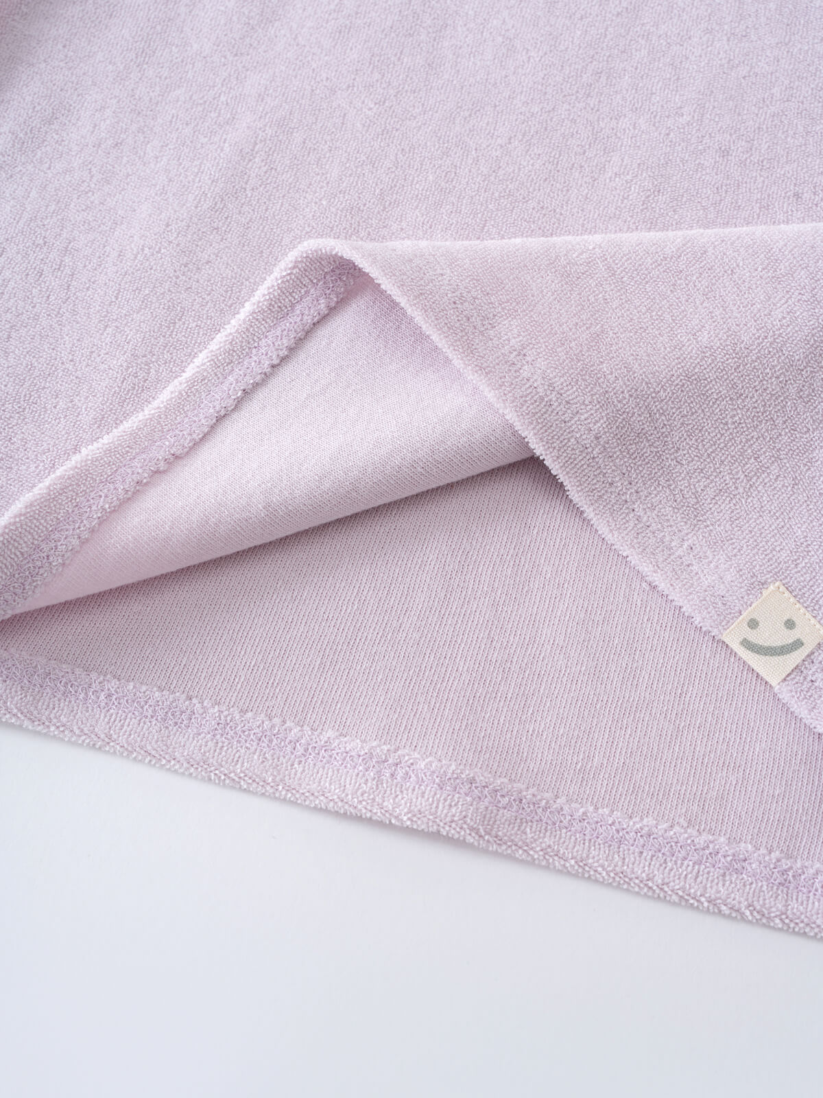 Close-up of a light purple towelling fabric with folded corner and tag Towelling Tee Shirt - Lilac Girls