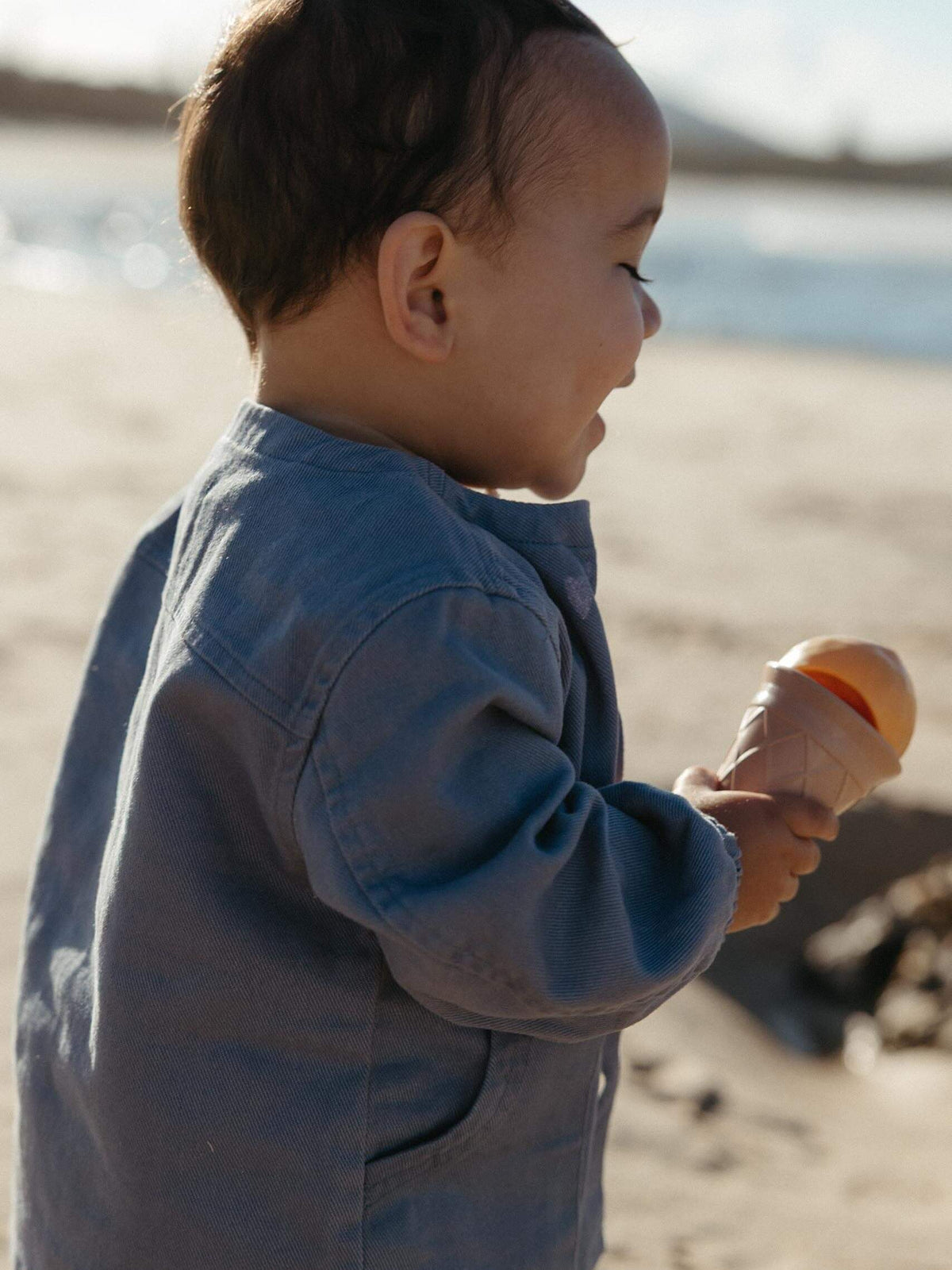 toddler playing at he beach wearing a blue denim jacket
