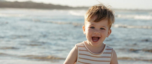 Baby standing on a beach in a sand stripe sleeveless jersey romper, from the Yes Mila baby rompers NZ range