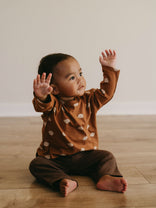 Young child sitting on wooden floor wearing rust-colored printed long sleeve top Baby Printed Long Sleeve Tee - Cosy Bear Russet Baby boy