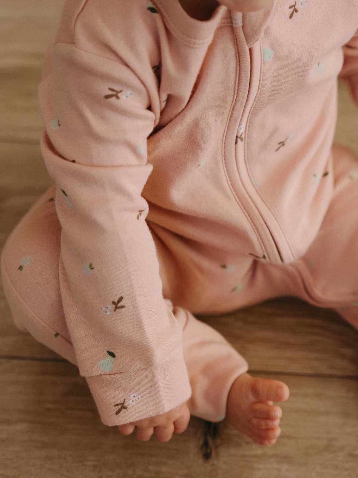 Baby wearing a pink printed onesie with zipper sitting on wooden floor Printed Long Sleeve One Piece - Autumn Harvest Rosehip Baby girl
