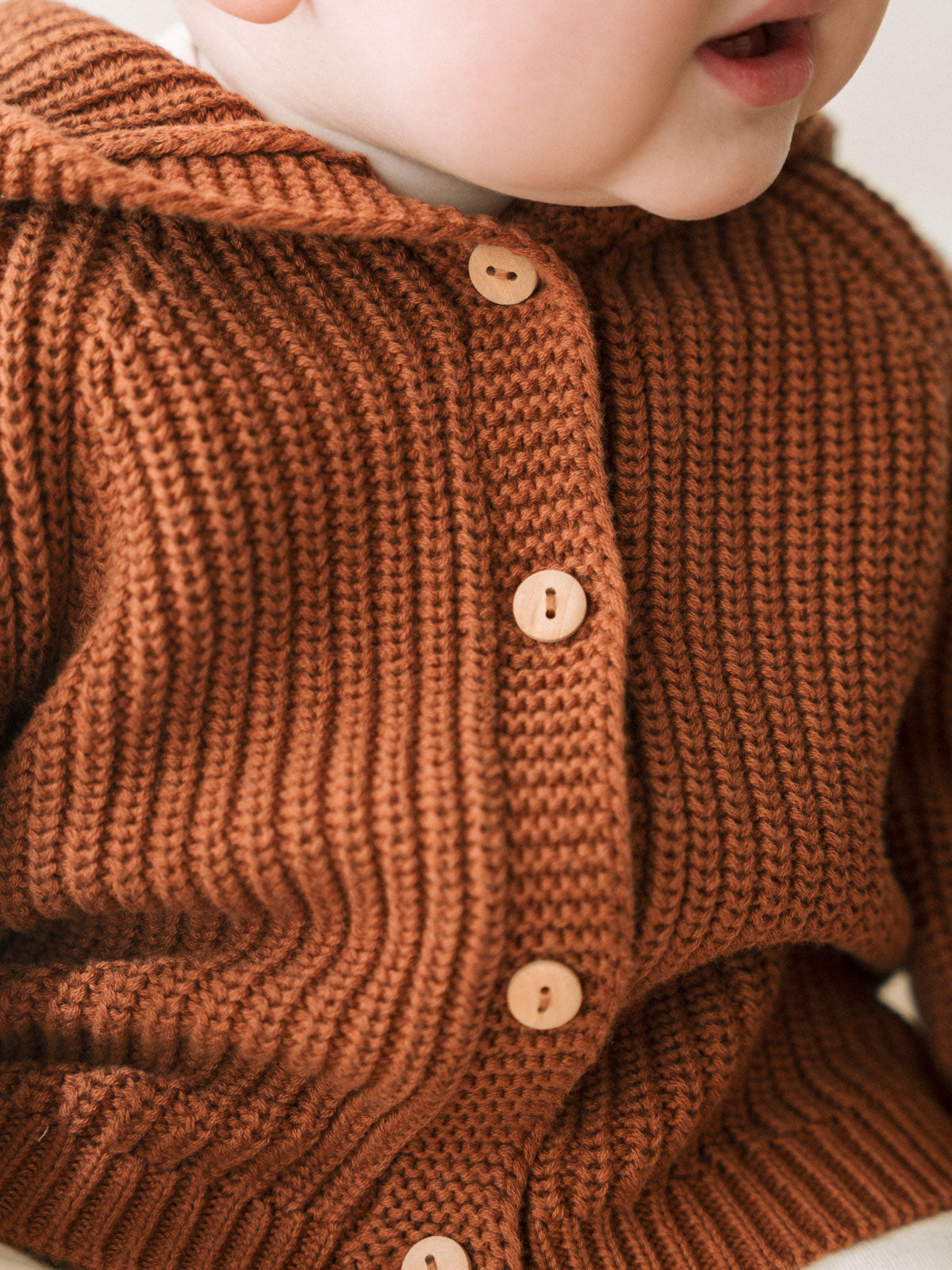 Close-up of a child wearing a rust-colored ribbed knit cardigan with buttons Ribbed Hooded Cardigan - Russet Baby boy