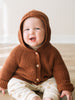 Baby wearing a rust-colored knitted hooded cardigan with wooden buttons sitting down Ribbed Hooded Cardigan - Russet Baby boy