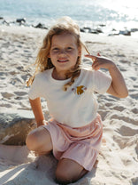 Girl at the beach smiling to the camera wearing a white tee and a pink skirt