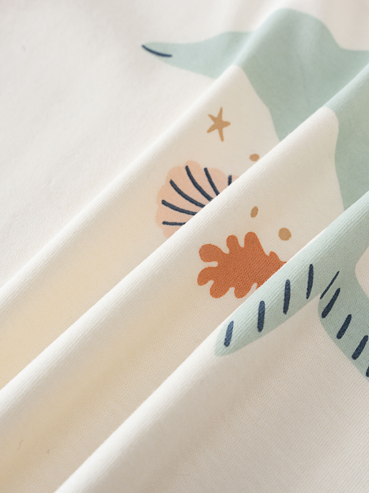 Close-up of folded fabric showing abstract shapes and patterns in cream and sage colors Feature Print Short Sleeve Tee - Dolphin Short Sleeve Tee Shirt - Dolphin Girls