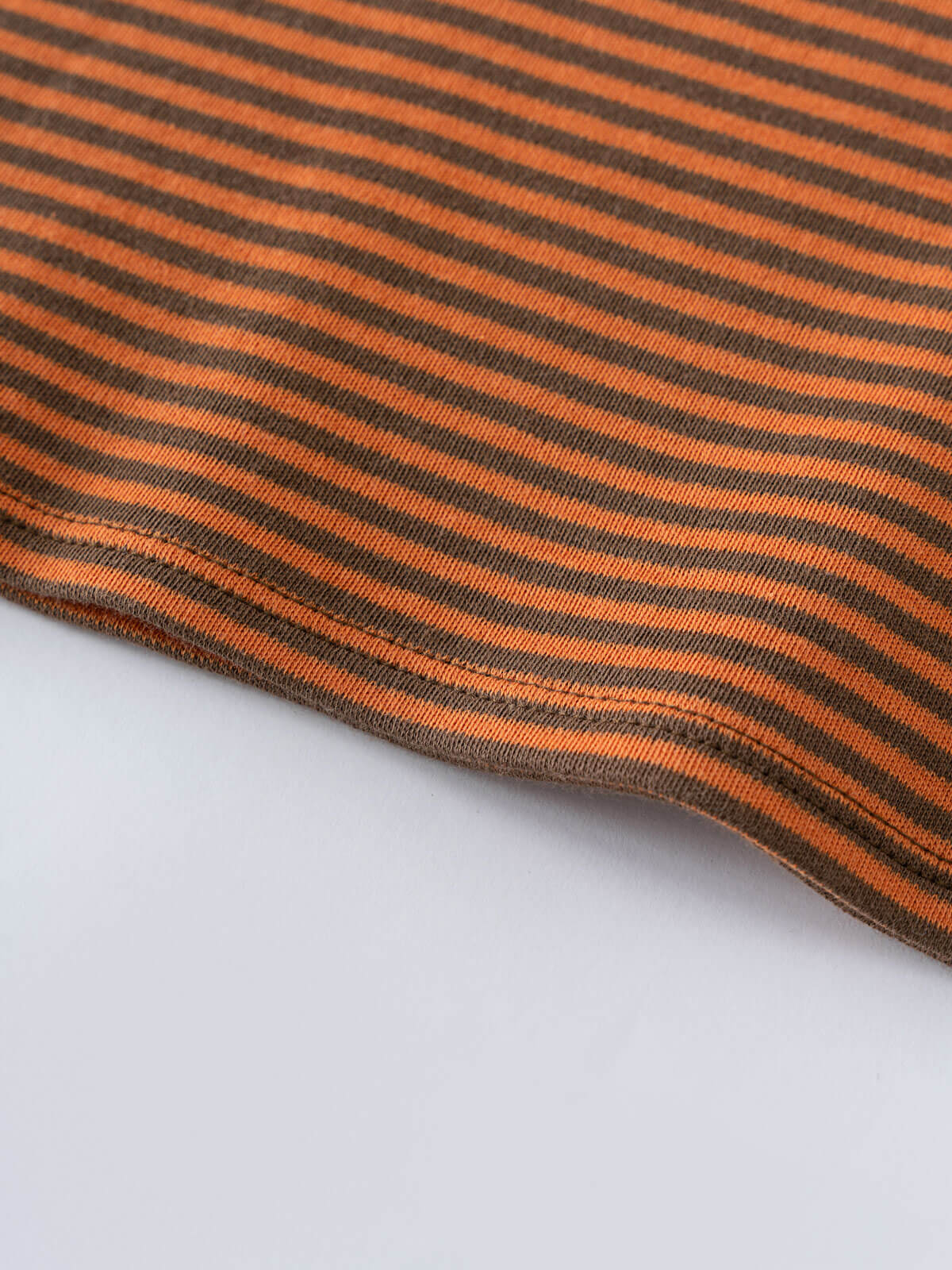 Close-up of orange and brown striped knit fabric with curved hem edge Henley Long Sleeve Tee - Pumpkin Boys