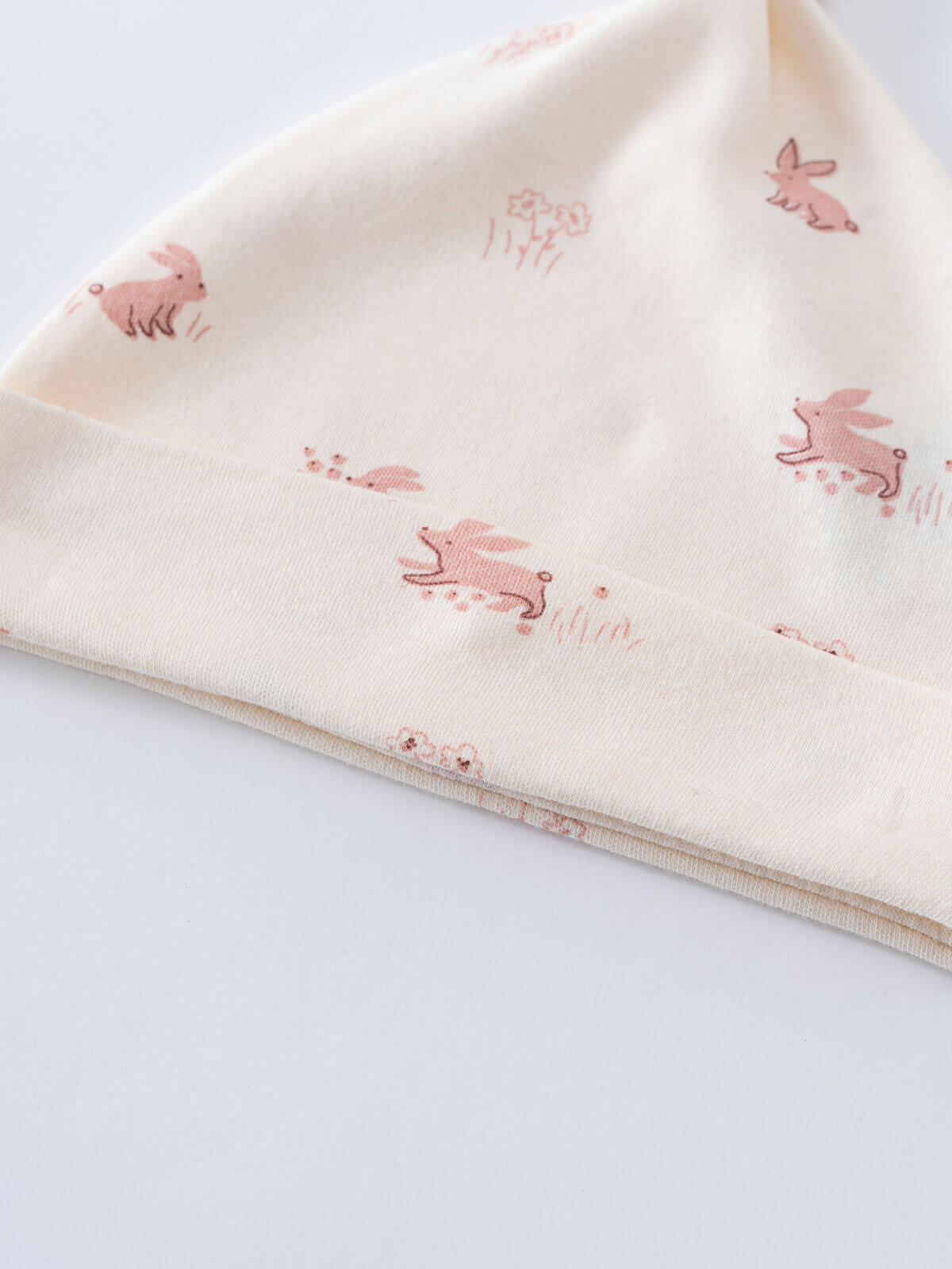 Close-up of cream fabric with small pink rabbit pattern print Knot Hat - Meadow Friends Ecru Baby girl