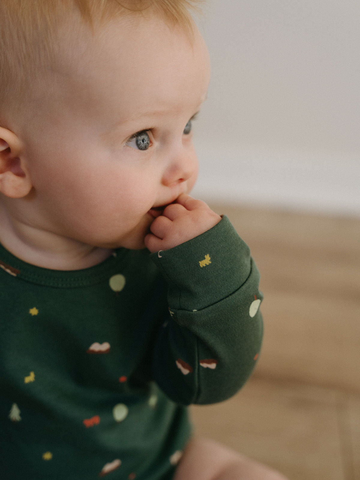 Blonde toddler in green patterned bodysuit with hand near mouth Long Sleeve Bodysuit - Mountain View Balsam Baby boy