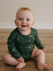 Baby in green patterned bodysuit sitting on wooden floor smiling Long Sleeve Bodysuit - Mountain View Balsam Baby boy