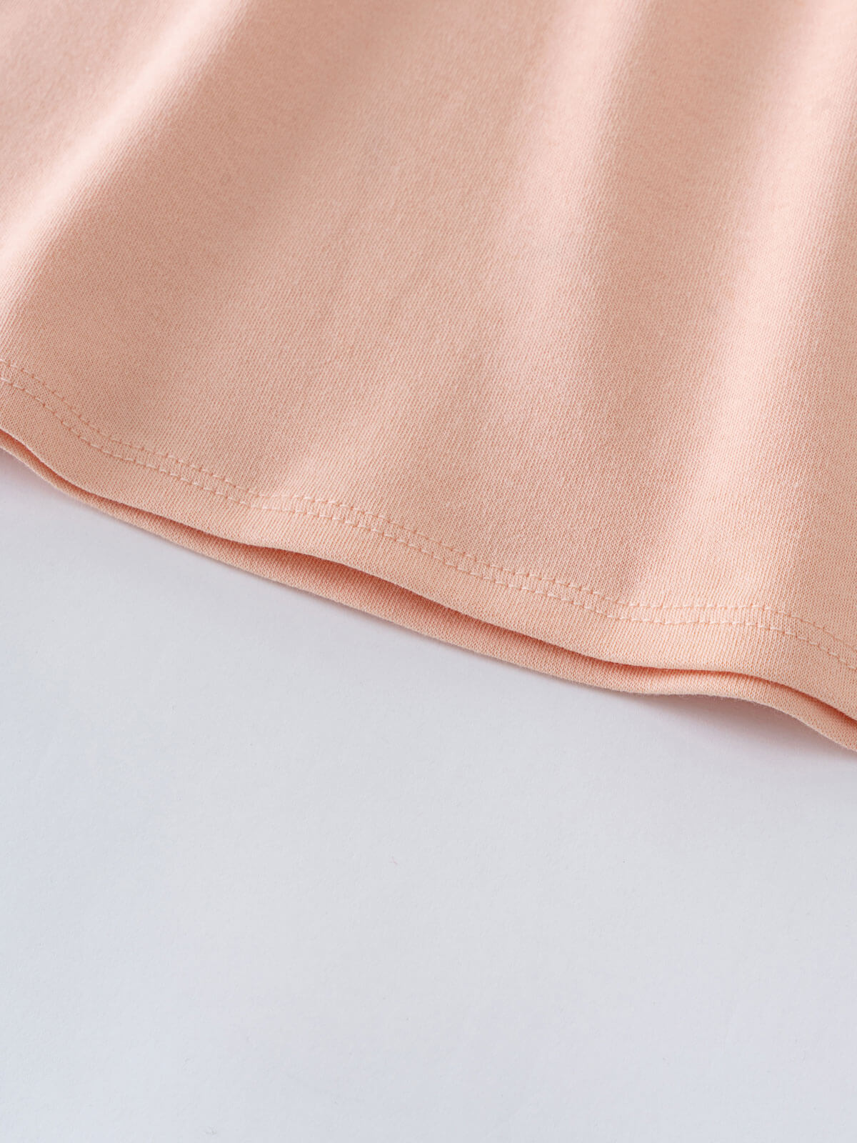Close-up of a peachy pink fabric hem with visible stitching detail Long Sleeve Jersey Dress - Mallow Girls