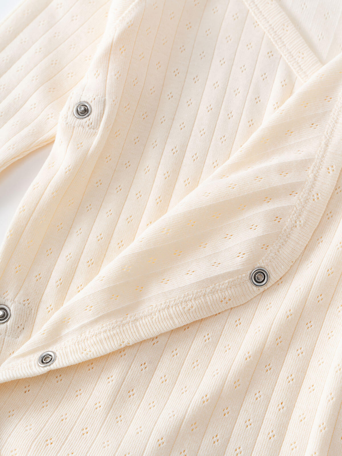 Close-up of cream-colored pointelle knit fabric with snap buttons Pointelle Crossover Bodysuit - Ecru Baby boy