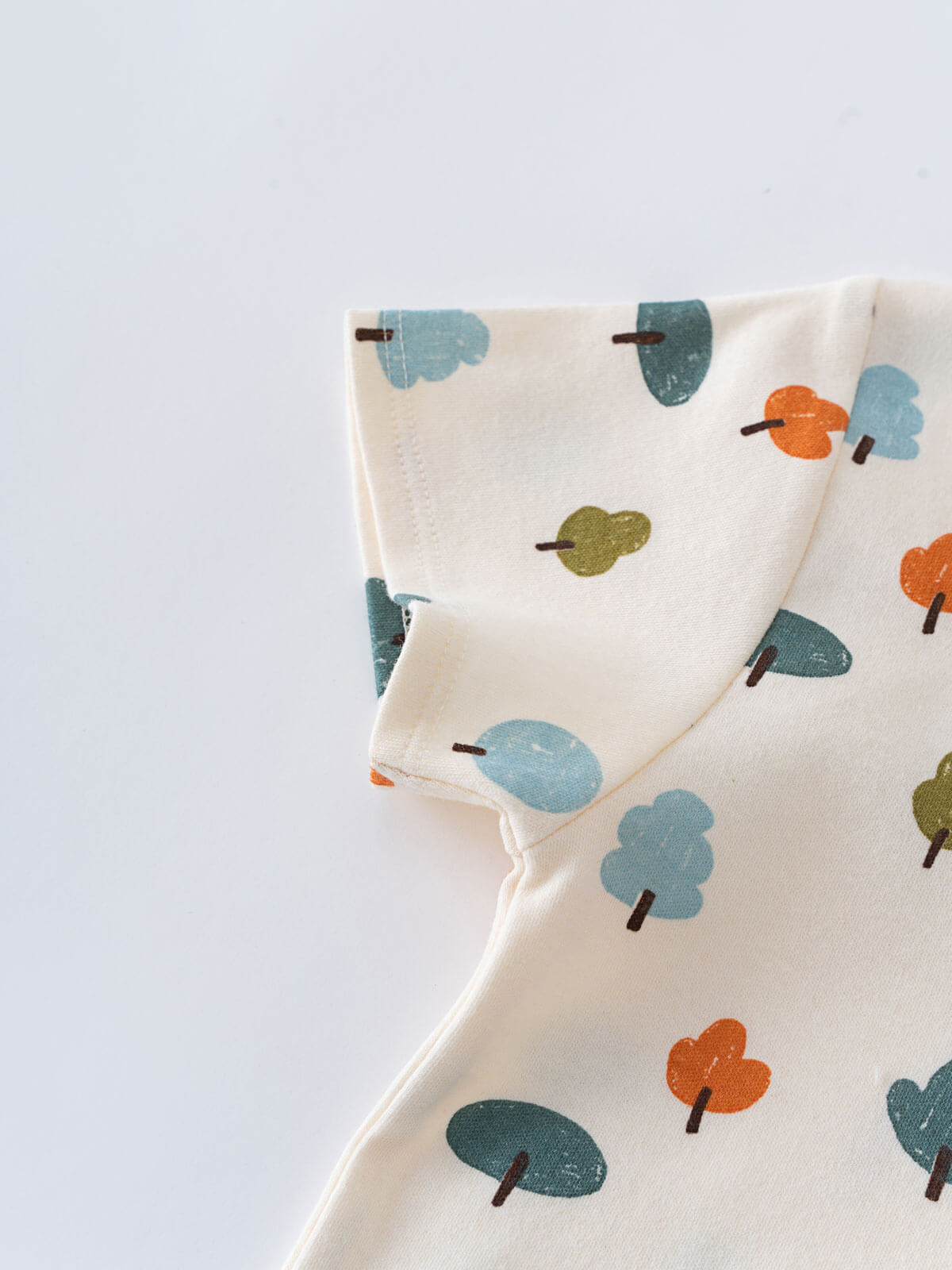Folded cream fabric with colorful tree pattern in blue, orange, and green Printed Short Sleeve Tee - Forest Adventure Ecru Boys