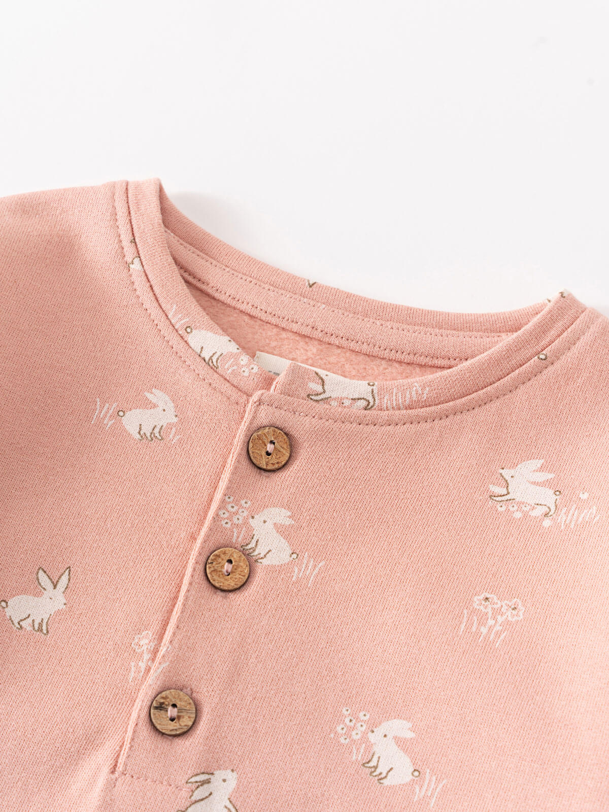 Close-up of pink fabric with white rabbit print and brown buttons Sweatshirt Onesie - Meadow Friends Blush Baby girl