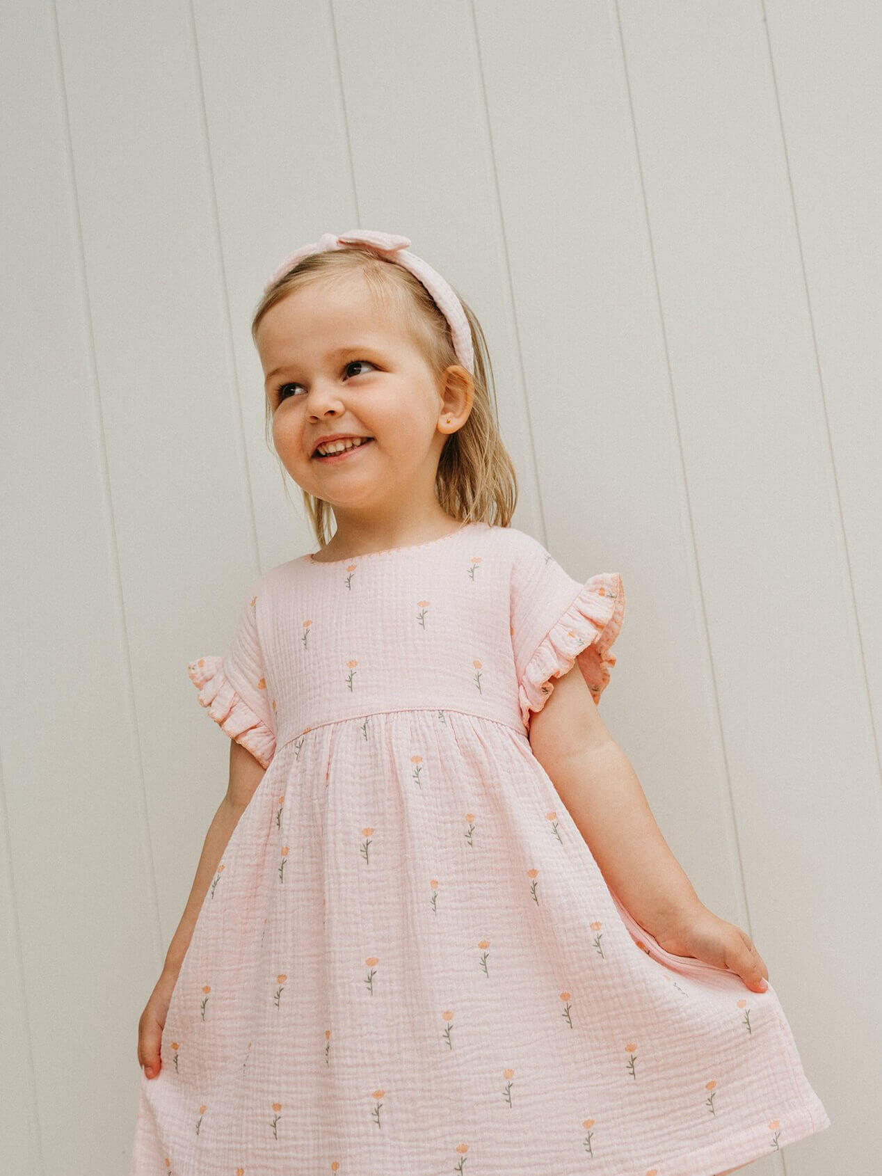Young girl wearing a pink dress with a subtle pattern against a light background
