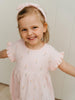 Young girl wearing a pink dress with ruffled sleeves and a matching headband, standing against a light background. Amara Dress - Poppy Field Girls