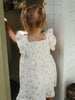 Child wearing a white floral dress standing in a doorway.