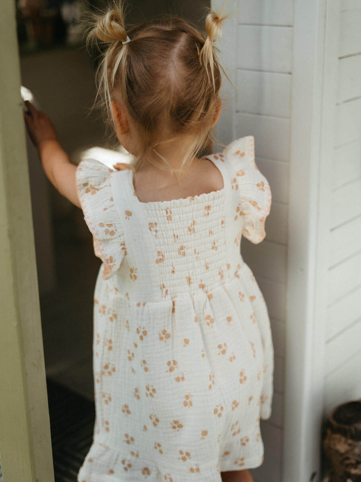 Child wearing a white floral dress standing in a doorway.