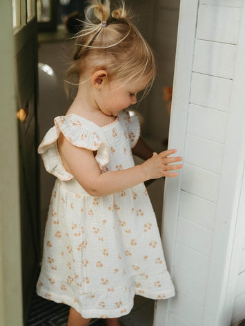 Young girl in a floral dress standing in a doorway. Amelia Dress - Petal Paws Baby girl