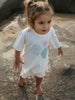 Child wearing a white t-shirt with a blue whale design on a rocky surface