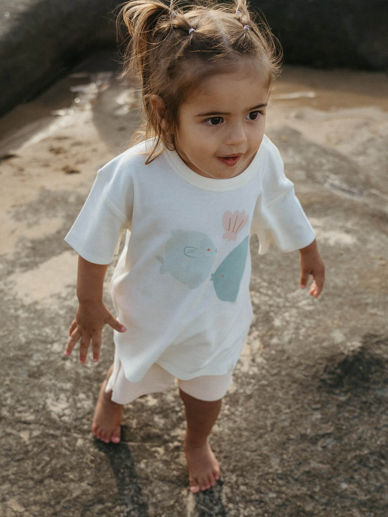 Child wearing a white t-shirt with a blue whale design on a rocky surface