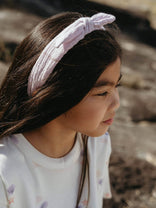 Young girl wearing a pink knotted headband with a blurred natural background