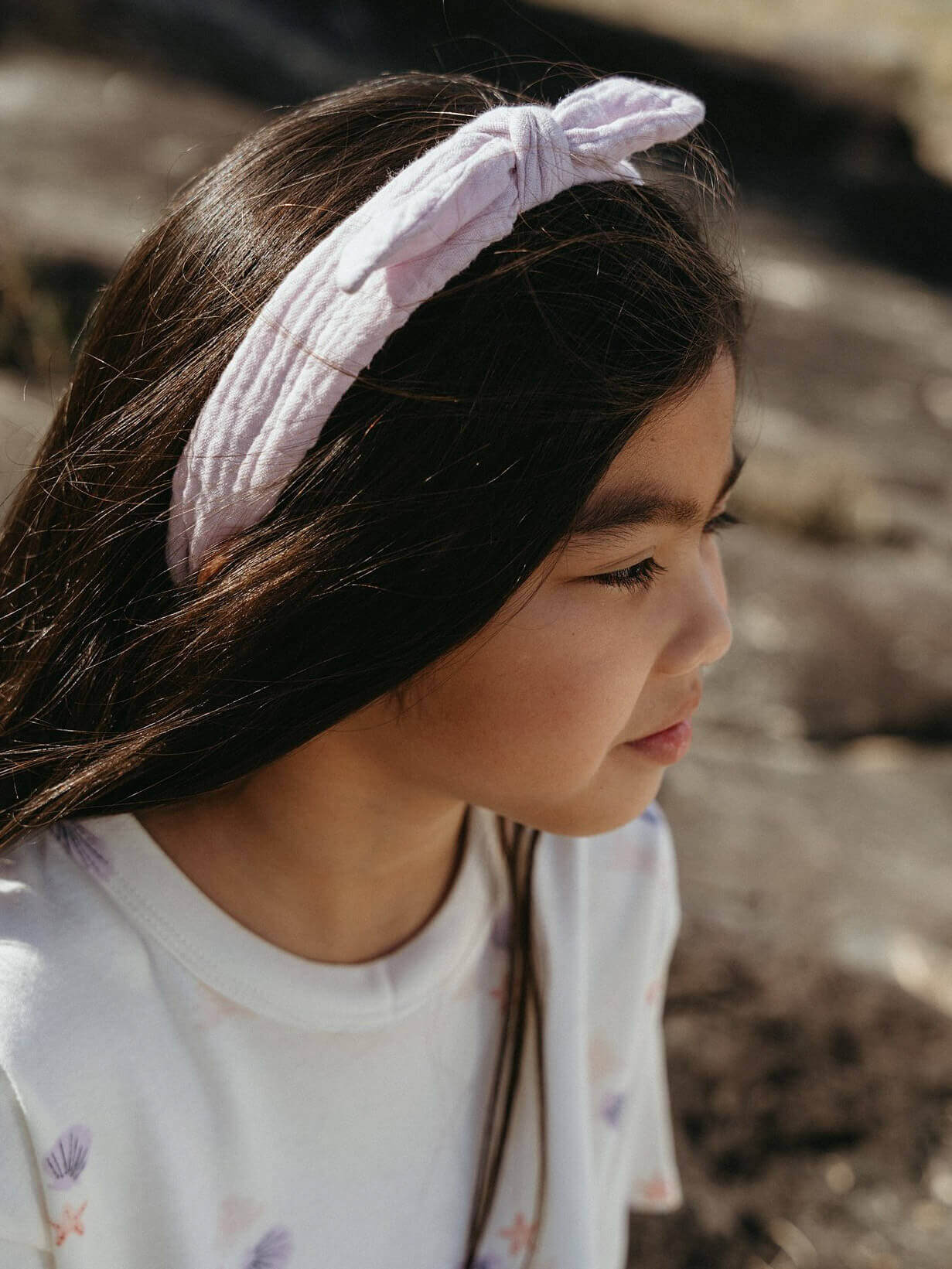 Young girl wearing a pink knotted headband with a blurred natural background