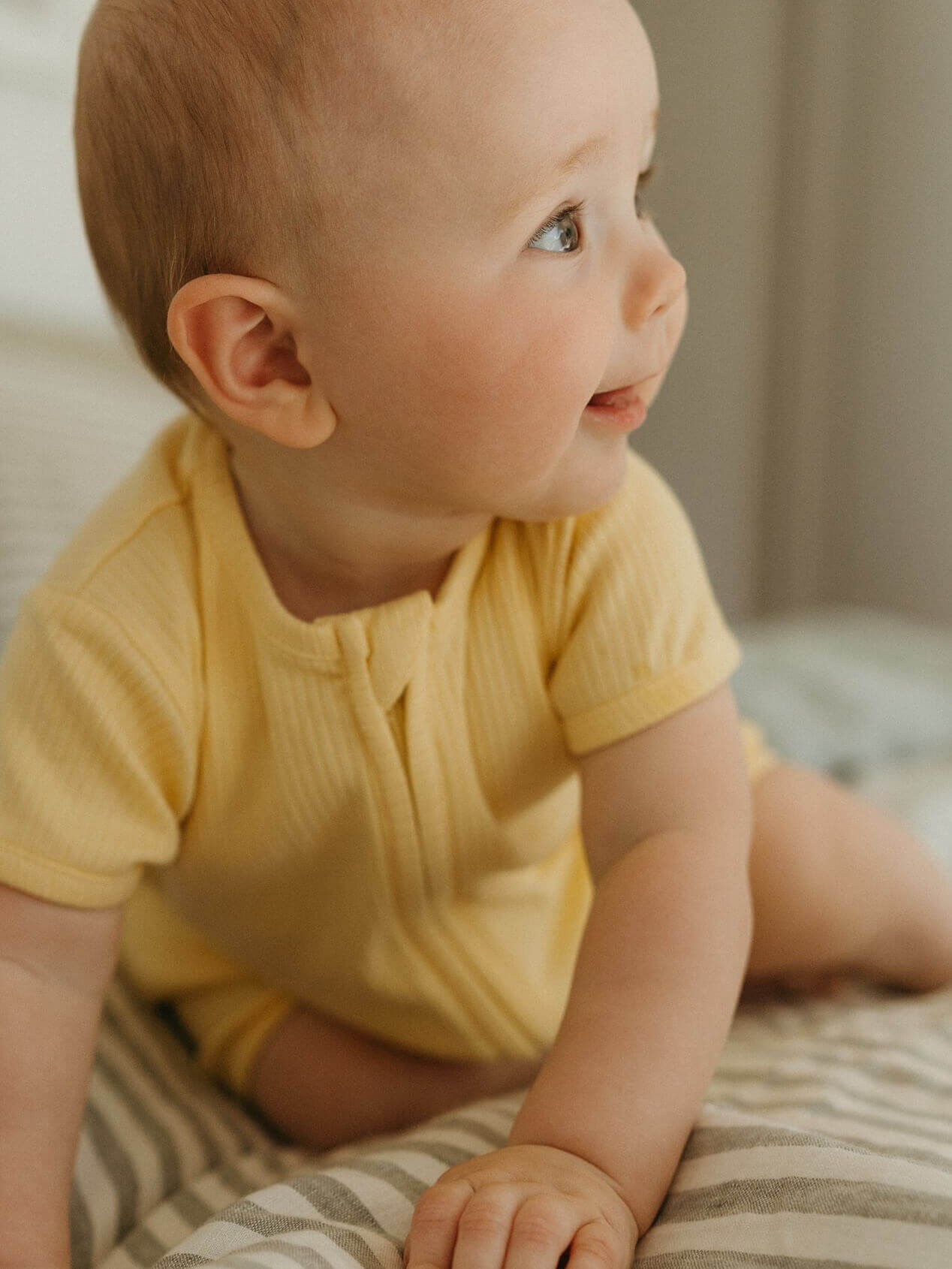 Baby in a yellow onesie sitting on a striped blanket