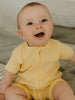 Baby wearing a yellow outfit sitting on a soft surface