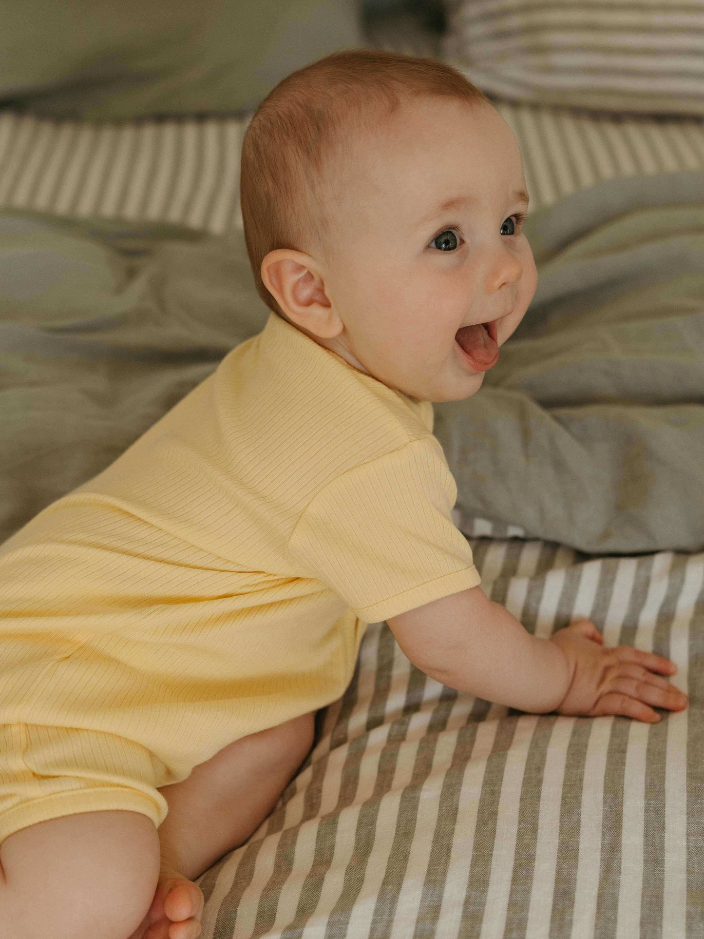 Baby in a yellow outfit sitting on a striped bed